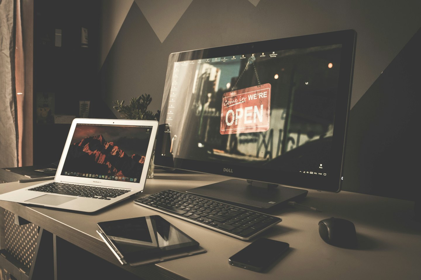 Scrivania moderna da ufficio con laptop e monitor su una parete geometrica.